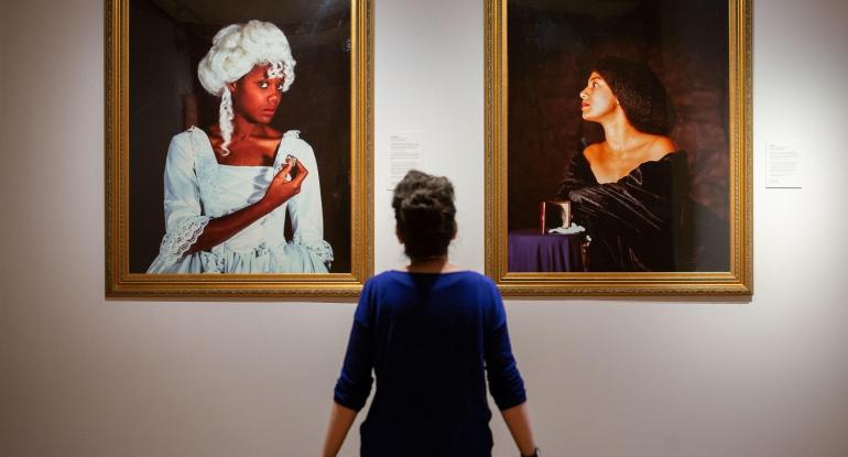 Curator sits admiring two paintings on display - both paintings are in gold frames