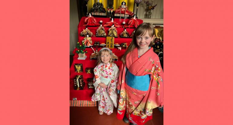 Two little girls wearing kimonos, standing in front of a display of Japanese artefacts