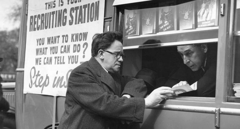 Photo of a man speaking through a hatch in a vehicle to another man