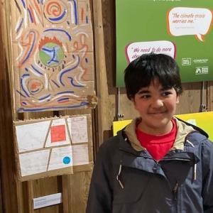 A child standing next to a cardboard sign made by him in the exhibition