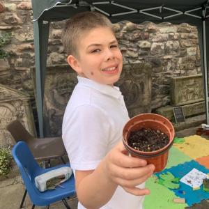 A boy holding out a plant pot and showing it to the camera