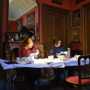 Two volunteers sitting in the dining room of Lauriston Castle polishing silver objects from the collection