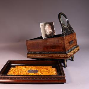 A cabinet card viewer, a wooden box with a stand magnifying glass and a stand for a cabinet card. Currently displaying a card with a Scottish outdoor scene.