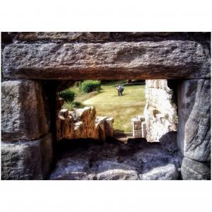 Colour photograph looking through a gap in a stone wall, with someone taking a photograph in the distance