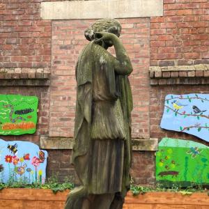 Four mural boards showing wildlife and plants in bright colours against a bricj wall with a statue of a woman in the foreground