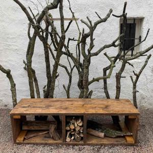 A wooden bench with tree branches used as a seat backing and an insect hotel underneath