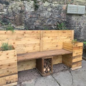 A wooden bench with insect hotel underneath and planters at the back and sides