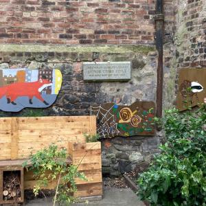 A wooden bench with three mural boards on the wall behind and next to it showing a fox, a hedgehog, badger and worms