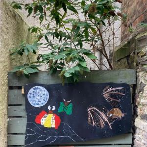 Image of a mural board showing a bat and moth against a fenced area and water butt